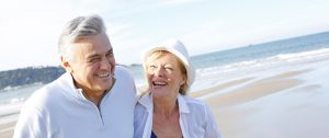 A midlife couple, a man and a woman, laughing together while standing on a sunny beach, enjoying a joyful moment by the ocean.